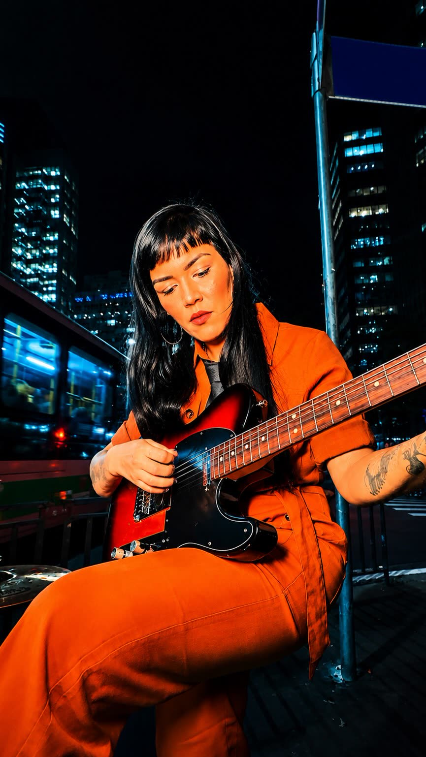 Guitarrista de macacão laranja tocando telecaster na noite de São Paulo