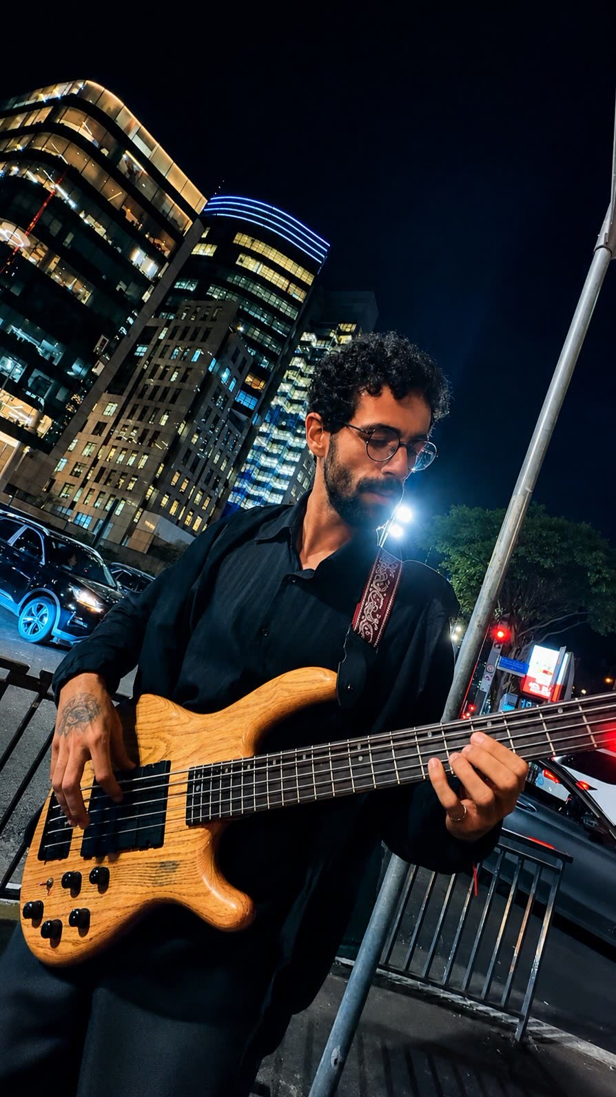 Baixista tocando na calçada entre prédios iluminados